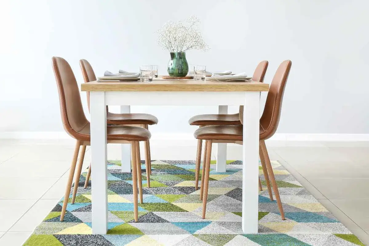 Tappeto sotto il tavolo da pranzo: sì! Un tappeto geometrico colorato aggiunge stile e comfort alla zona pranzo con sedie in pelle marrone.