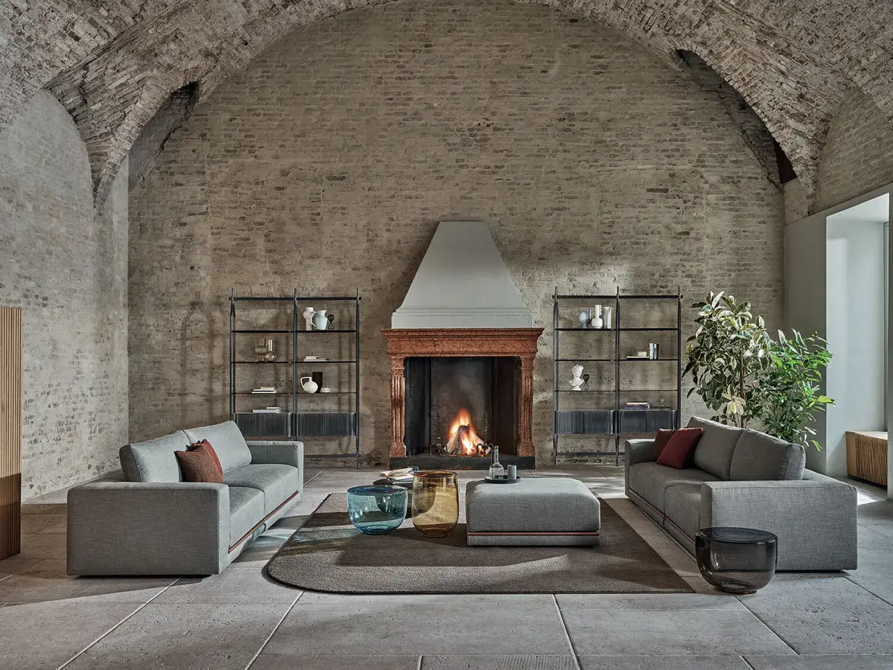Scegliere tappeto salotto: un'elegante zona living con divani grigi, camino acceso e tavolini moderni su un tappeto rotondo.