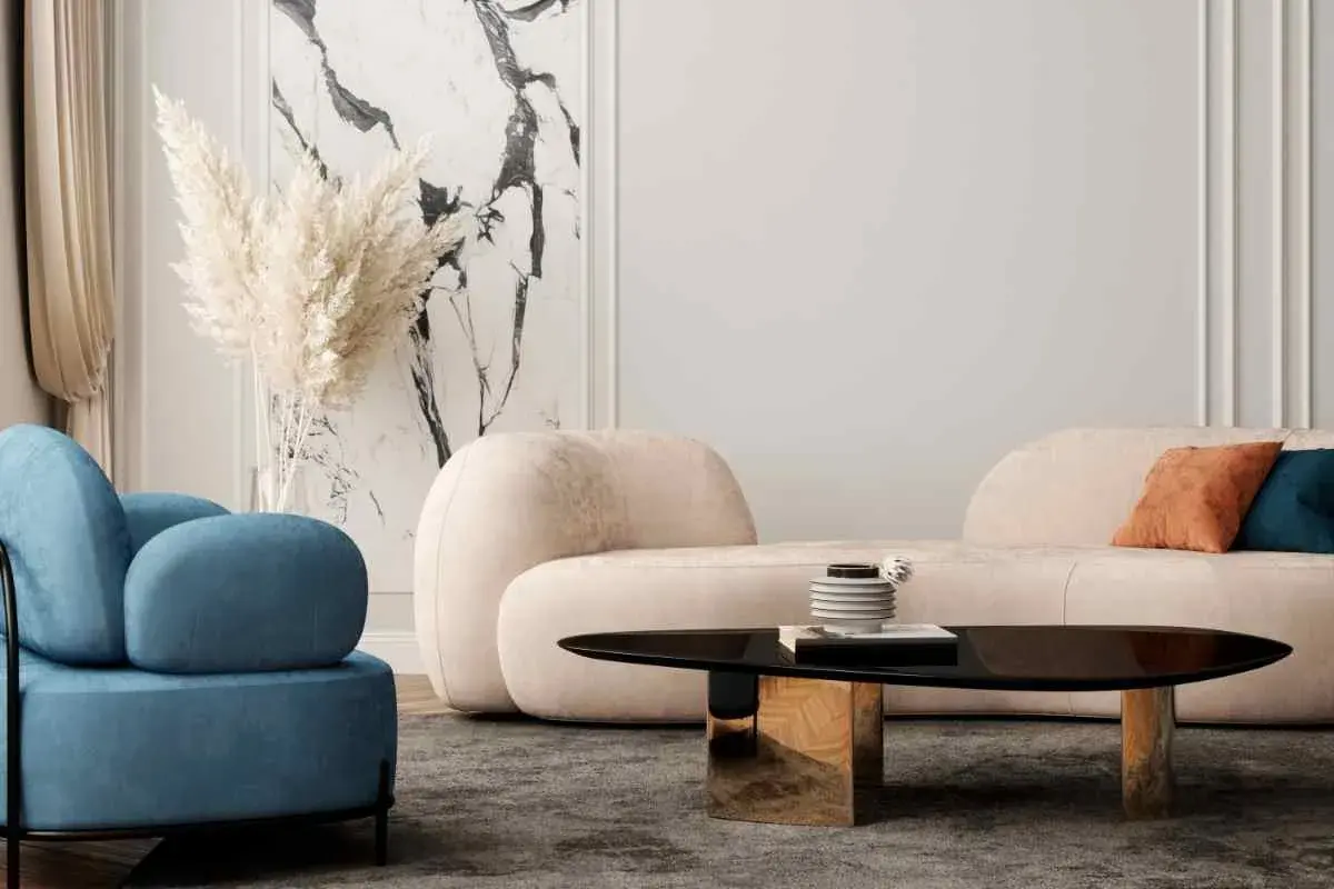 Un accogliente soggiorno con un divano beige, pareti chiare e una poltrona blu. Un tavolino nero lucido con base dorata completa l'arredamento.
