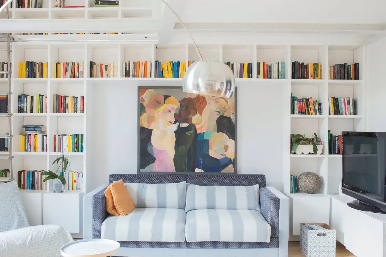 Divano a righe davanti a una libreria bianca piena di libri e un quadro colorato.