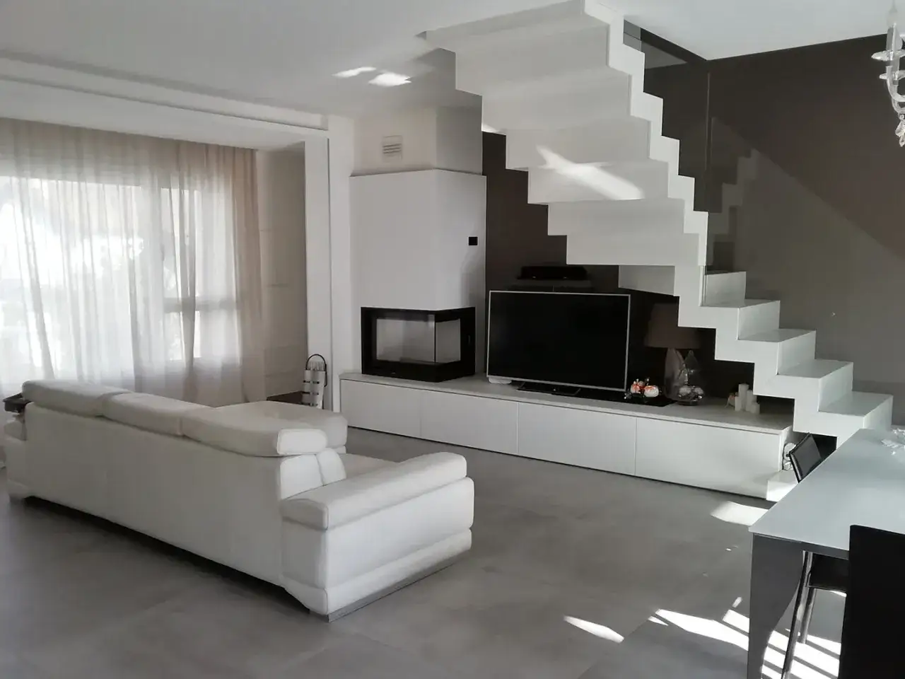 Soggiorno moderno con divano bianco, camino e scala a vista. Ottime idee arredare soggiorno con scala a vista per un design unico.