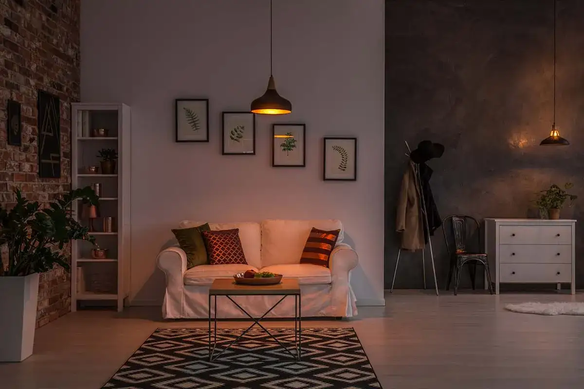 Soggiorno accogliente con divano bianco, tappeto geometrico e lampade che creano un'atmosfera calda, perfetti colori per stanze poco luminose.
