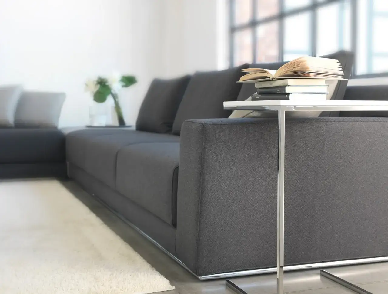 Divano moderno in tessuto grigio, con cuscini morbidi e un tavolino con libri. Il materiale alcantara dona un tocco di lusso.