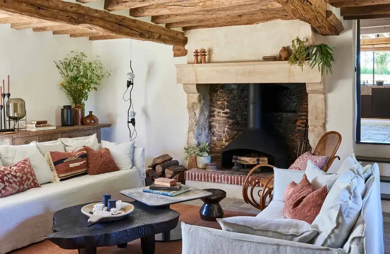 Accogliente soggiorno con travi a vista e camino in pietra, che crea ambienti rustici e caldi. Divani comodi e tavolini in legno grezzo completano l'arredo.