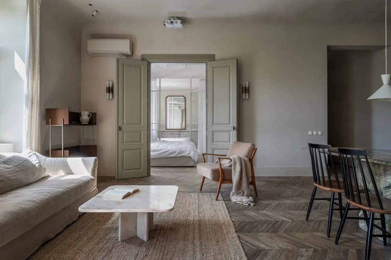 Un accogliente soggiorno con un tappeto su parquet chiaro, divano, poltrona e un libro aperto sul tavolino.