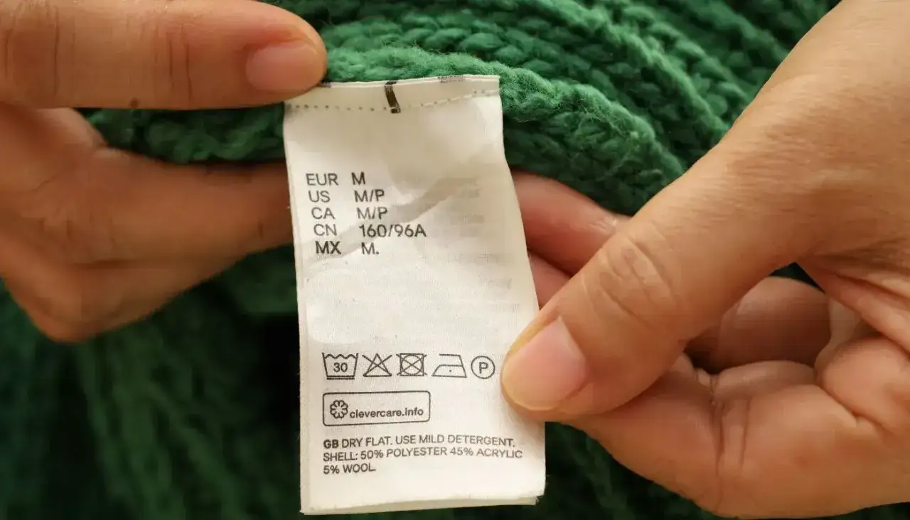 Etichetta di un maglione verde: lavaggio a 30 gradi, non candeggiare, asciugare in piano. La lana si lava a 30 gradi.