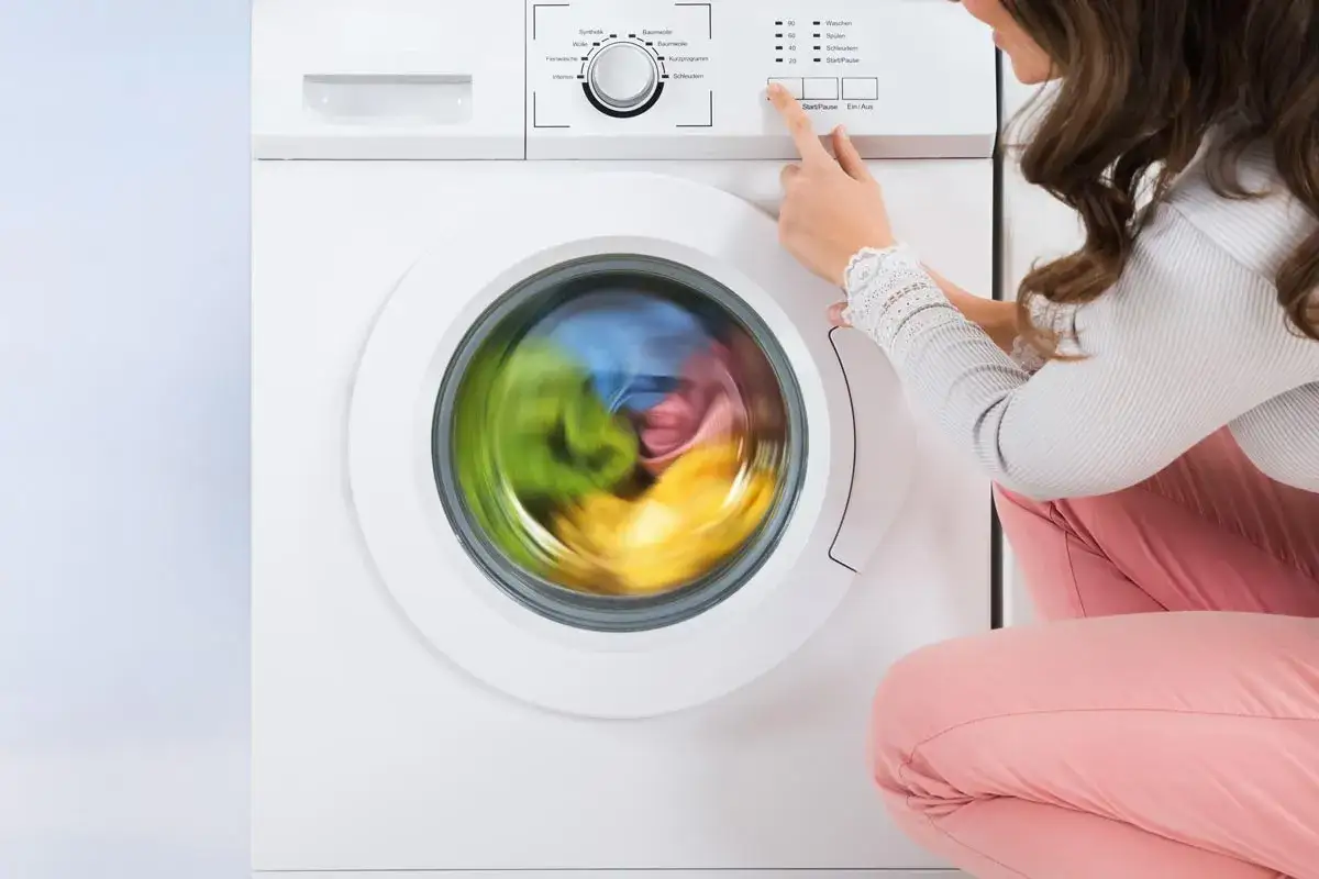 Donna avvia la lavatrice, il cestello gira velocemente con panni colorati. Si imposta la durata centrifuga lavatrice.