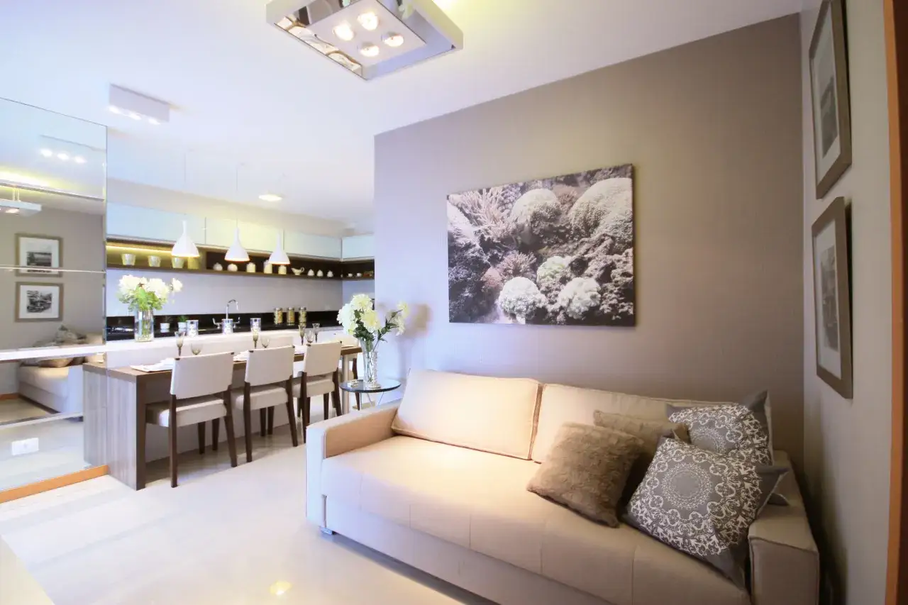 Divano beige accogliente, con cuscini decorativi, davanti a pareti color tortora e un quadro marino. La cucina moderna è visibile sullo sfondo.
