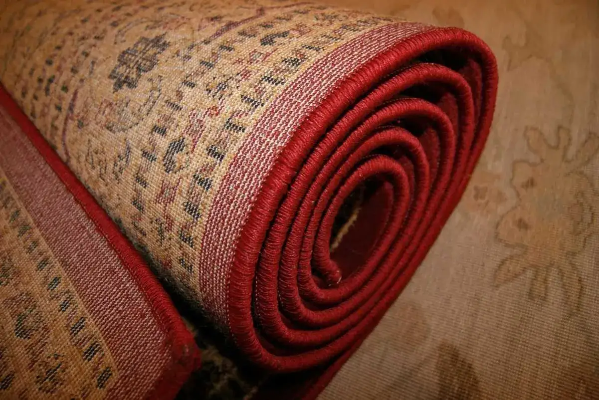 Dettaglio di un tappeto persiano arrotolato, con bordo rosso vivo. Consigli su come conservare i tappeti persiani per preservarne la bellezza.