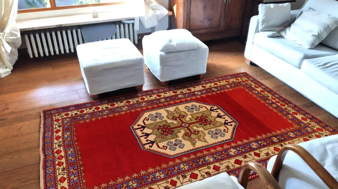 Un tappeto rosso con motivi geometrici, che evoca l'autenticità dei tappeti rustici, arreda un salotto moderno con divano bianco e pouf.