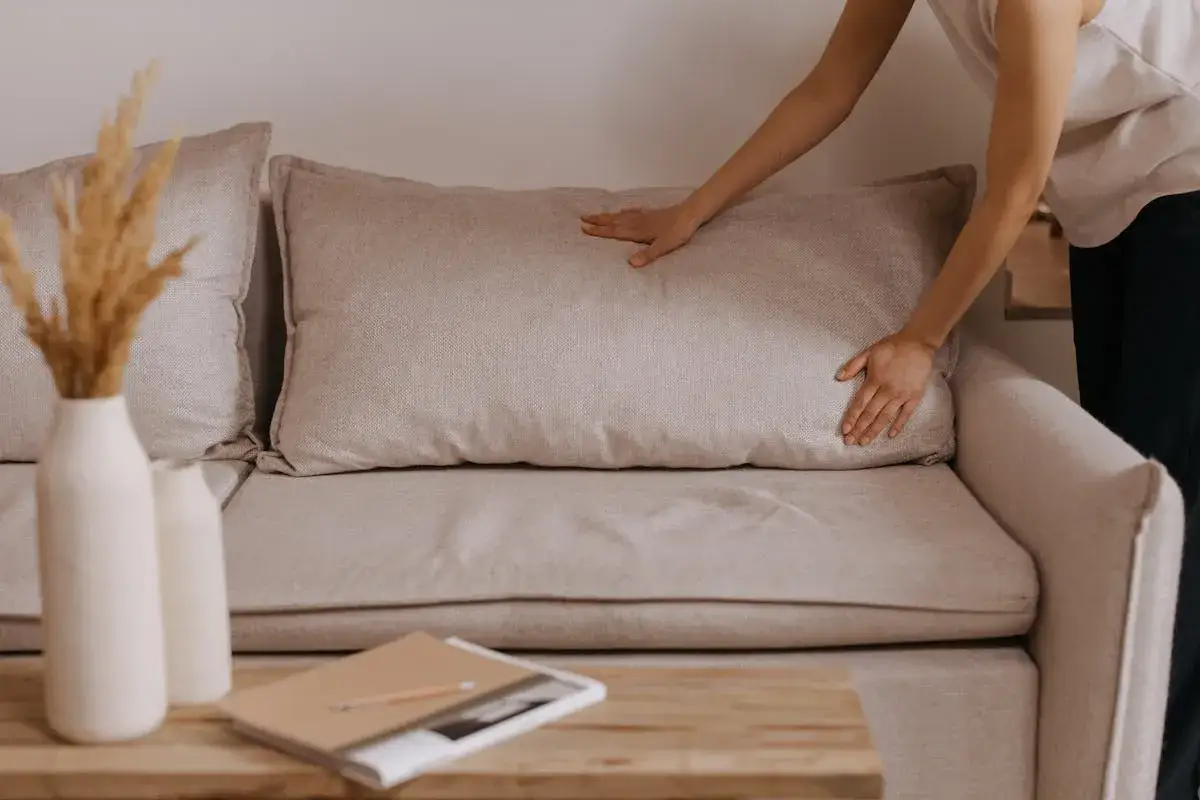 Mani che sistemano un cuscino su un divano beige, un'idea per rivestire divano fai da te.