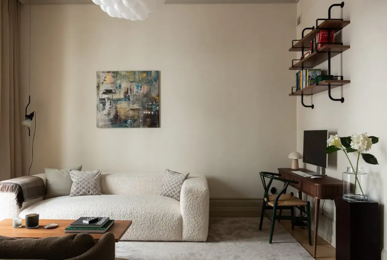 Divano beige su pareti color crema, con quadro astratto e scrivania con computer.