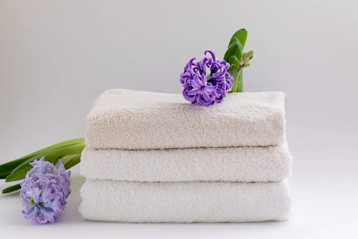 Morbidi asciugamani bianchi e beige impilati, decorati con giacinti viola. Un'ispirazione su come far profumare il bucato in modo naturale.