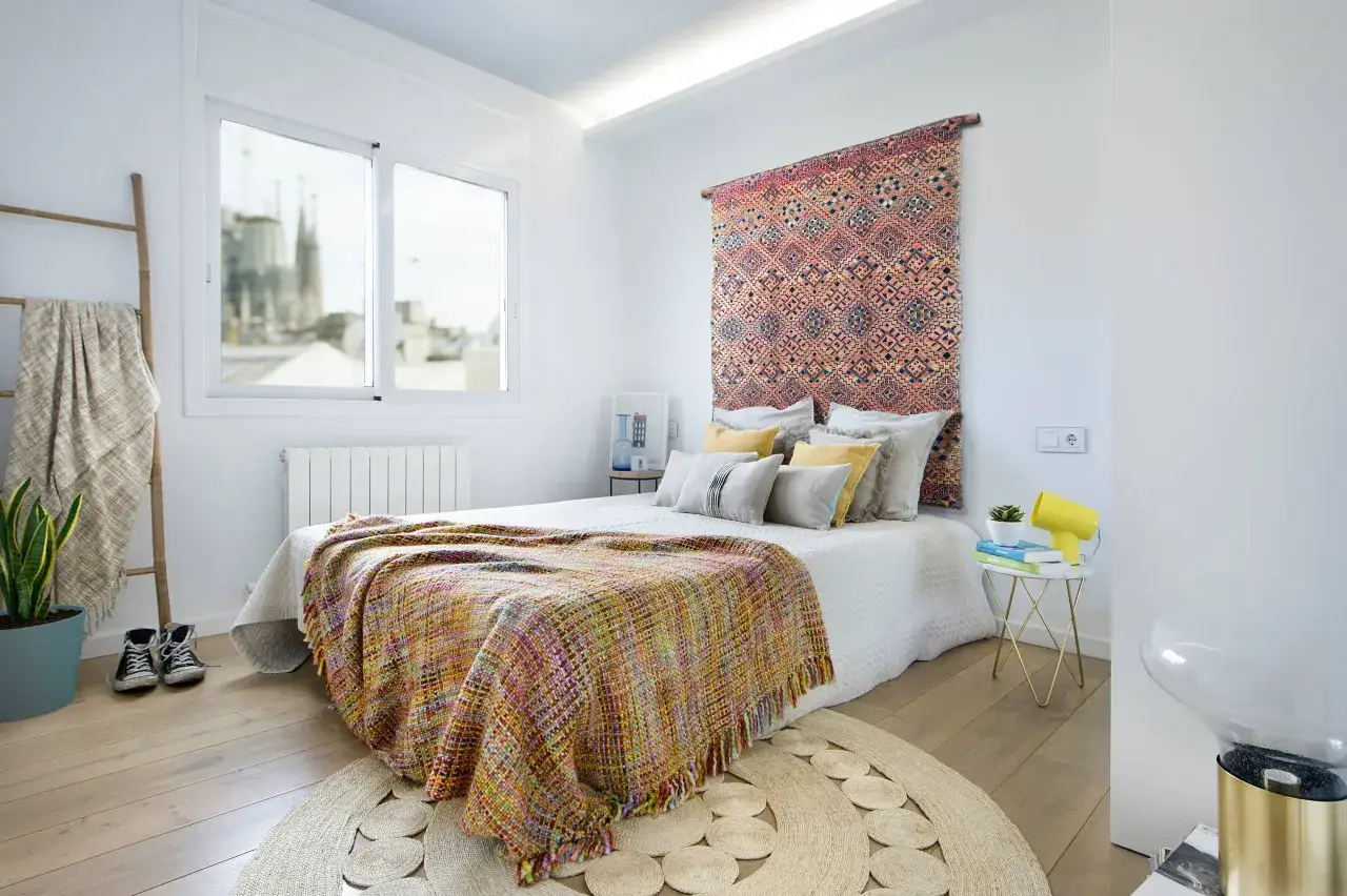 Un tappeto colorato appeso al muro sopra il letto, un'idea per come appendere un tappeto al muro con stile.