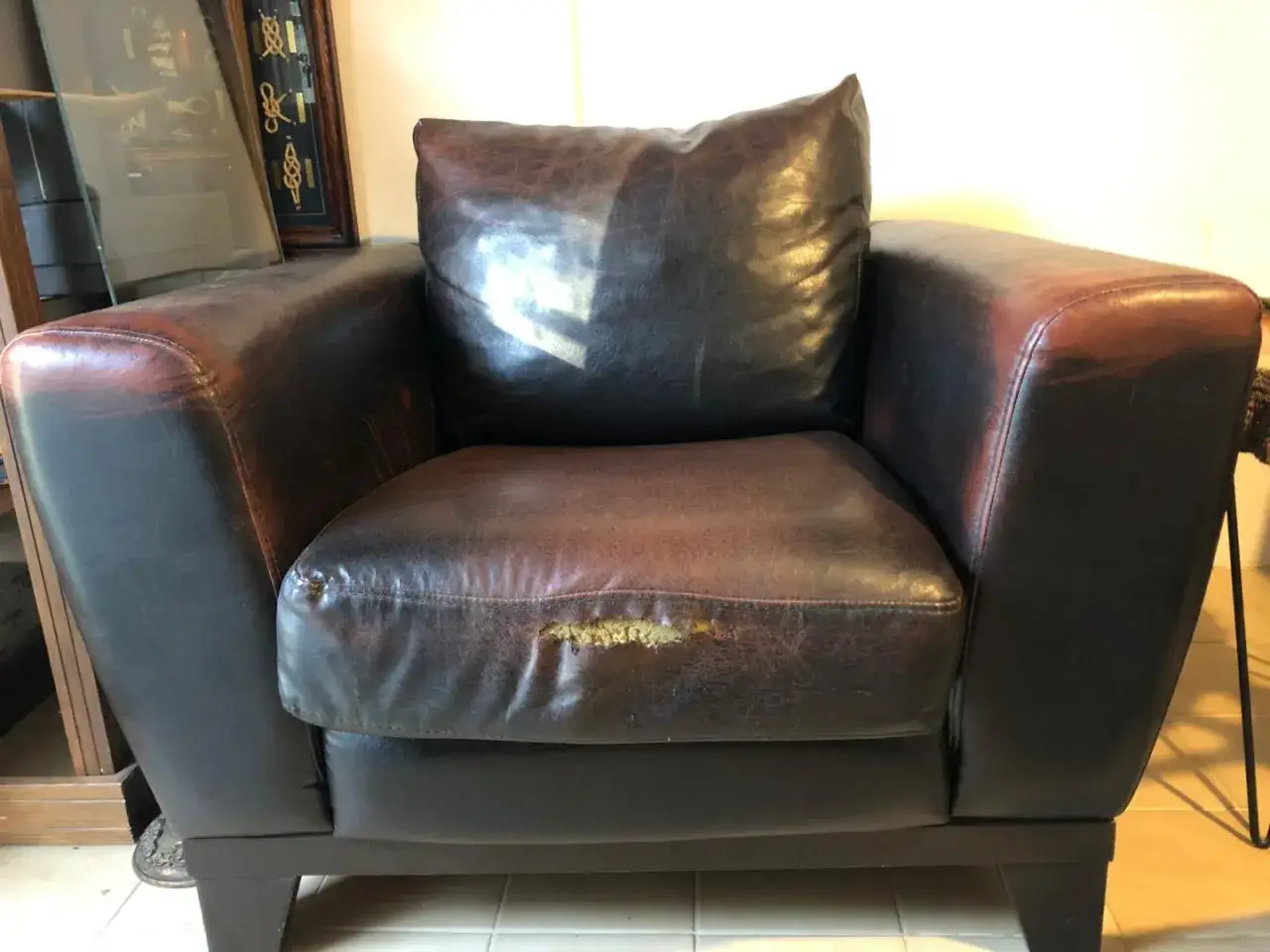 Poltrona in pelle marrone con un evidente buco sulla pelle del sedile, segno di usura.
