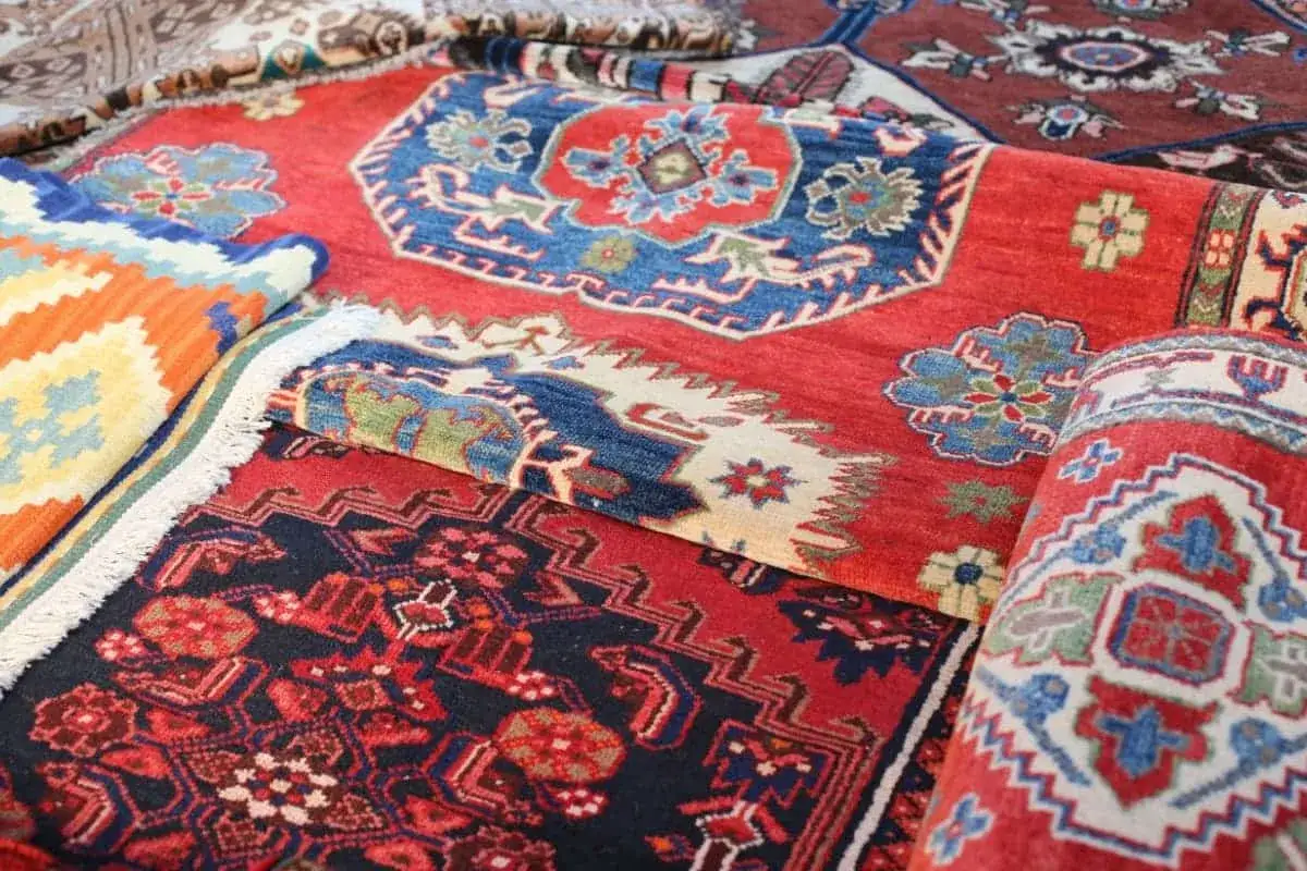 Vari tipi di tappeti persiani, con disegni geometrici e floreali in rosso, blu e giallo, mostrano la ricchezza dei motivi tradizionali.