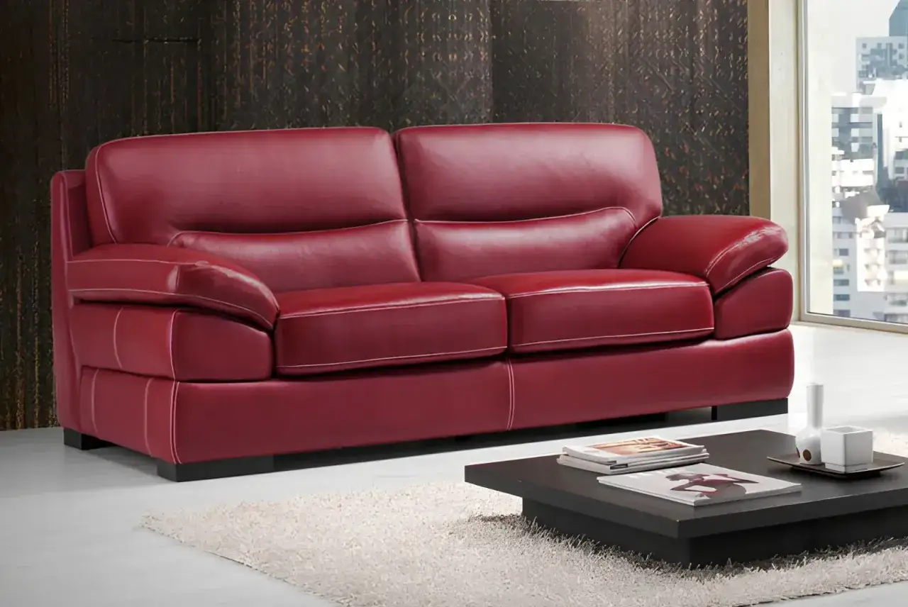 Divano rosso in pelle pull-up, con cuciture a contrasto, su un tappeto bianco.