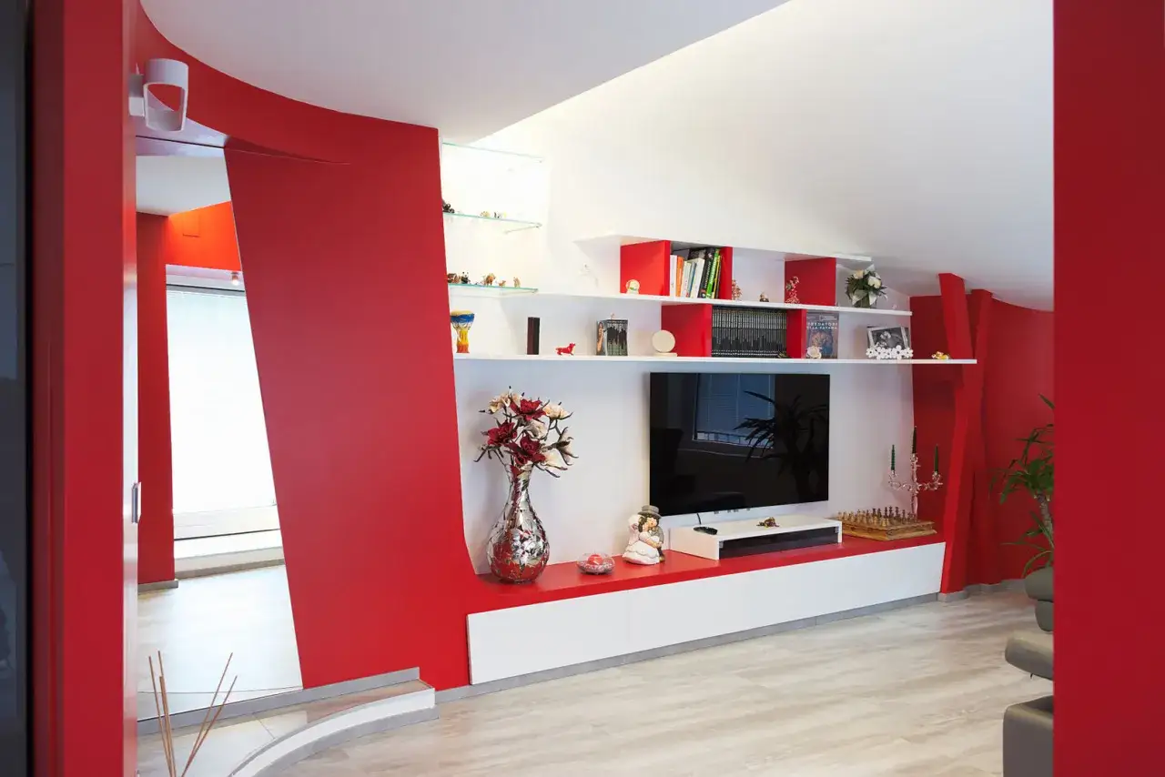 Pareti soggiorno rosso e grigio con mobili bianchi e rossi, TV, scaffali con libri e decorazioni.