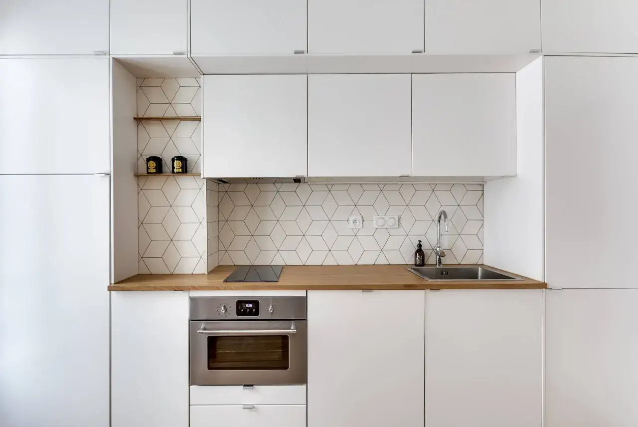 Moderna cucina bianca con paraschizzi a esagoni geometrici, piano in legno e forno a incasso. Idee per paraschizzi cucina bianca.