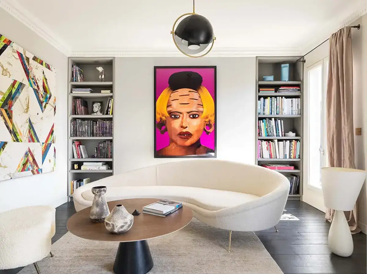 Un accogliente divano bianco al centro di una piccola stanza, con un tavolino e opere d'arte colorate.