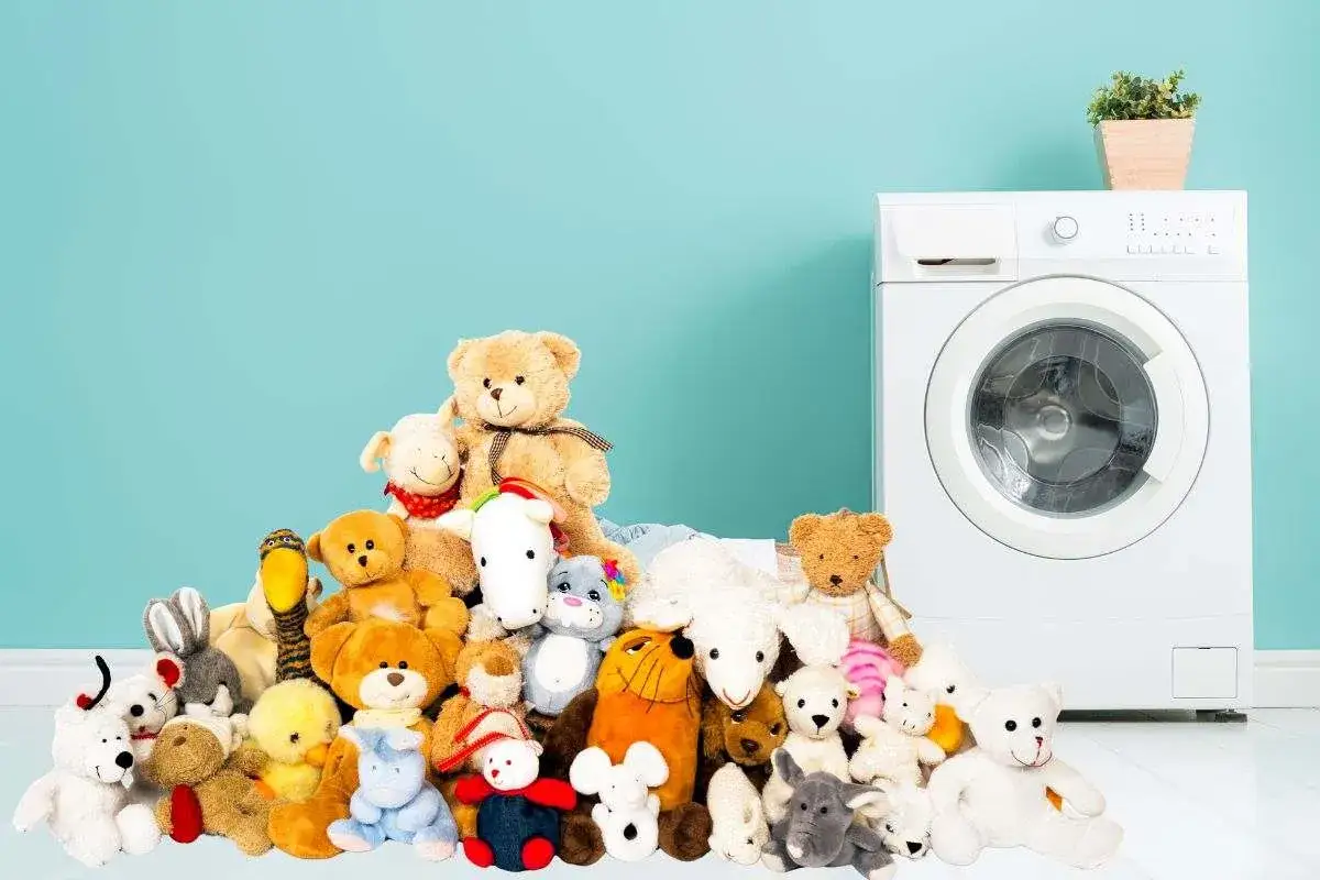 Un mucchio di peluche colorati attende di scoprire come lavare i peluche in lavatrice, accanto a una lavatrice bianca.