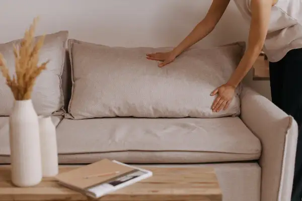 Mani che sistemano un cuscino su un divano beige, un'idea per rivestire divano fai da te.