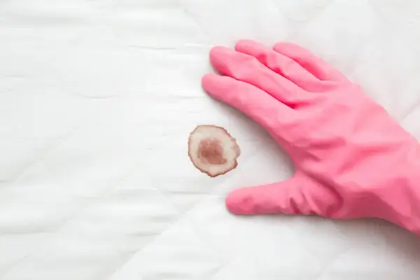 Mano con guanto rosa pronto a pulire macchie di sangue su tessuto bianco trapuntato.