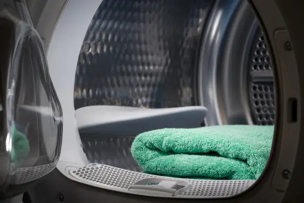 Interno di una lavasciuga con un asciugamano verde piegato. Si vede il cestello metallico e la porta trasparente.
