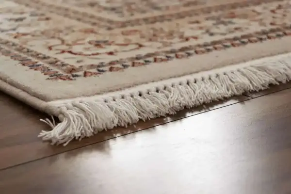 Dettaglio di un tappeto con frange bianche su parquet lucido. Scopri come pulire i tappeti per mantenerli splendenti.