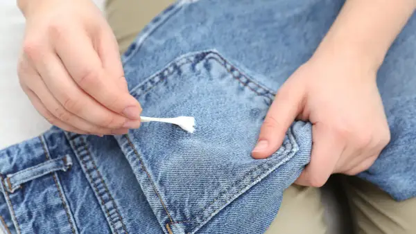 Mani che rimuovono la cingomma dai jeans con un cotton fioc. Ecco come togliere la cingomma dai vestiti.