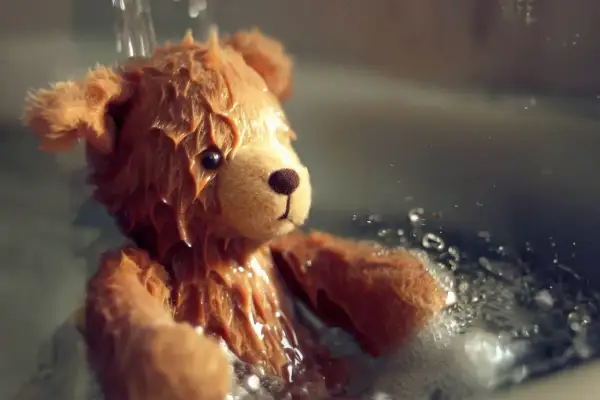 Orsetto di peluche bagnato, con gocce d'acqua che scendono. Una scena che ricorda come lavare i peluche in lavatrice per farli tornare come nuovi.