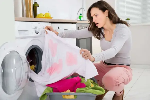 Donna scopre con orrore macchie rosse su un capo bianco appena lavato, un classico problema di come eliminare le macchie da trasferimento di colore rosso.