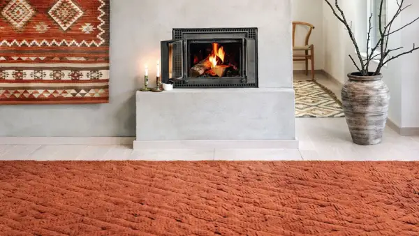 Un tappeto decorativo con motivi geometrici arancioni e bianchi è appeso al muro, un'idea per come appendere un tappeto al muro.