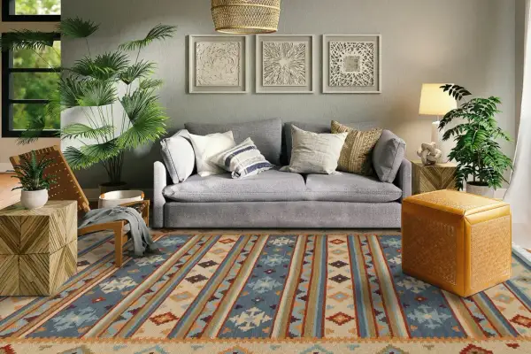 Tappeto 2 metri per 3 con motivi geometrici in blu, beige e arancione, che copre il pavimento di un soggiorno moderno con divano grigio e piante verdi.