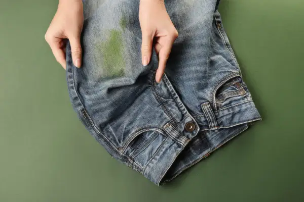 Mani che indicano una macchia verde su jeans, per mostrare come togliere macchie di jeans su ecopelle.