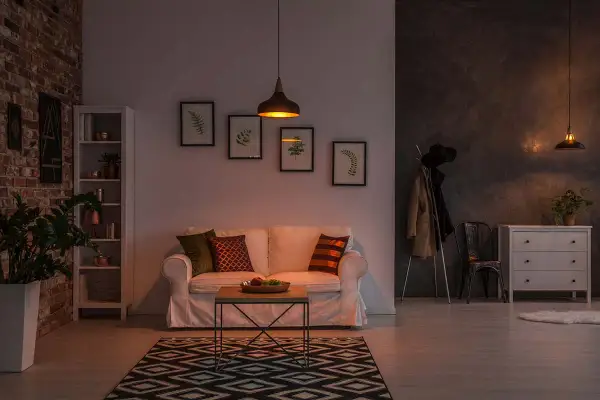 Soggiorno accogliente con divano bianco, tappeto geometrico e lampade che creano un'atmosfera calda, perfetti colori per stanze poco luminose.