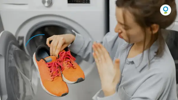 Donna con scarpe arancioni vicino a una lavatrice, con espressione disgustata. Scopri come profumare la lavatrice per un bucato fresco.