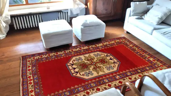 Un tappeto rosso con motivi geometrici, che evoca l'autenticità dei tappeti rustici, adorna il pavimento in legno di un soggiorno accogliente.