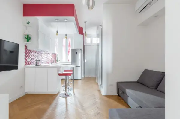 Un accogliente open space di 20 mq con cucina moderna, divano grigio e dettagli rossi vivaci.