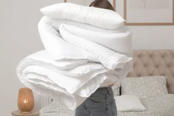 Donna con un grande piumone bianco, pronto per lavare copriletto in lavatrice. La biancheria da letto è piegata in modo ordinato.