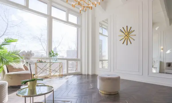 Un elegante soggiorno con un tavolino rotondo dorato, un pouf beige e un orologio a muro dorato a forma di sole.