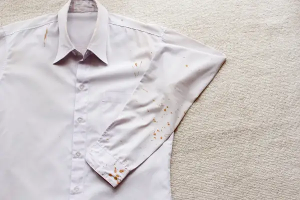 Camicia bianca con macchie di ruggine vecchie sui tessuti, soprattutto sulla manica e sul colletto.