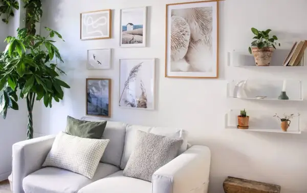 Galleria di quadri e mensole bianche sopra un divano bianco, con piante e oggetti decorativi. Idee mensole sopra divano per un tocco di stile.