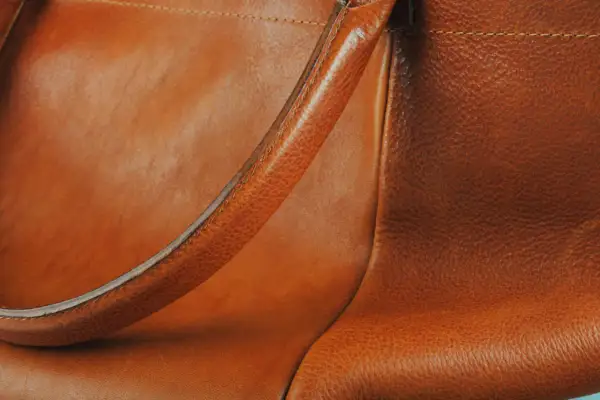 Dettaglio di una borsa in pelle marrone, con la texture del materiale che mostra lievi graffi sulla pelle, testimoni di un uso vissuto.