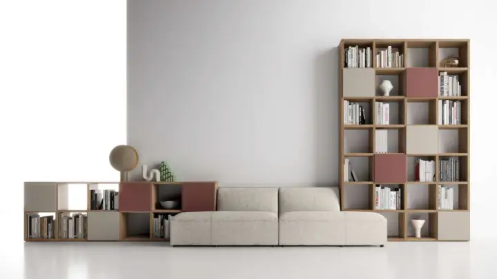 Un comodo divano beige è posizionato davanti a una libreria modulare in legno, piena di libri e oggetti decorativi.
